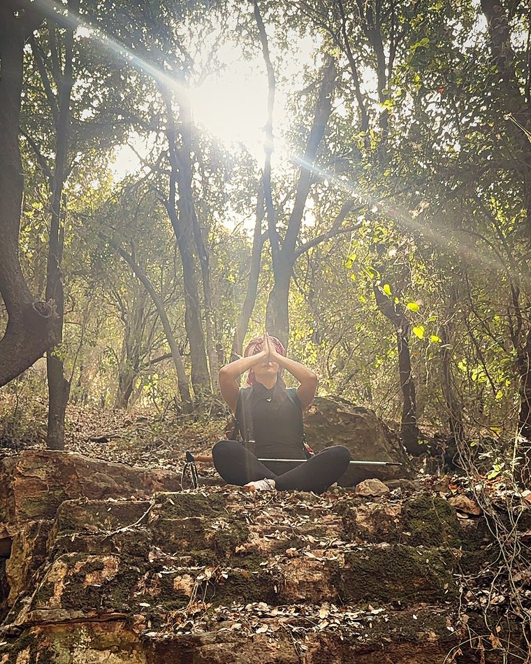 Sahar meditating on the old stone ledge as the sun breaks through the trees